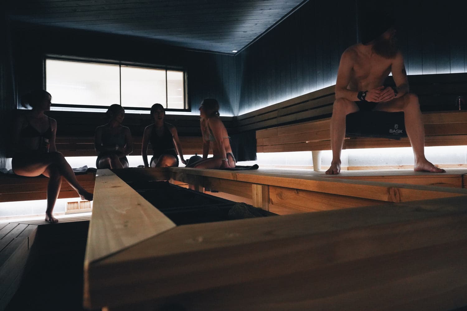 Guests relaxing in BASK Detroit dark cedar sauna with ambient bench lighting