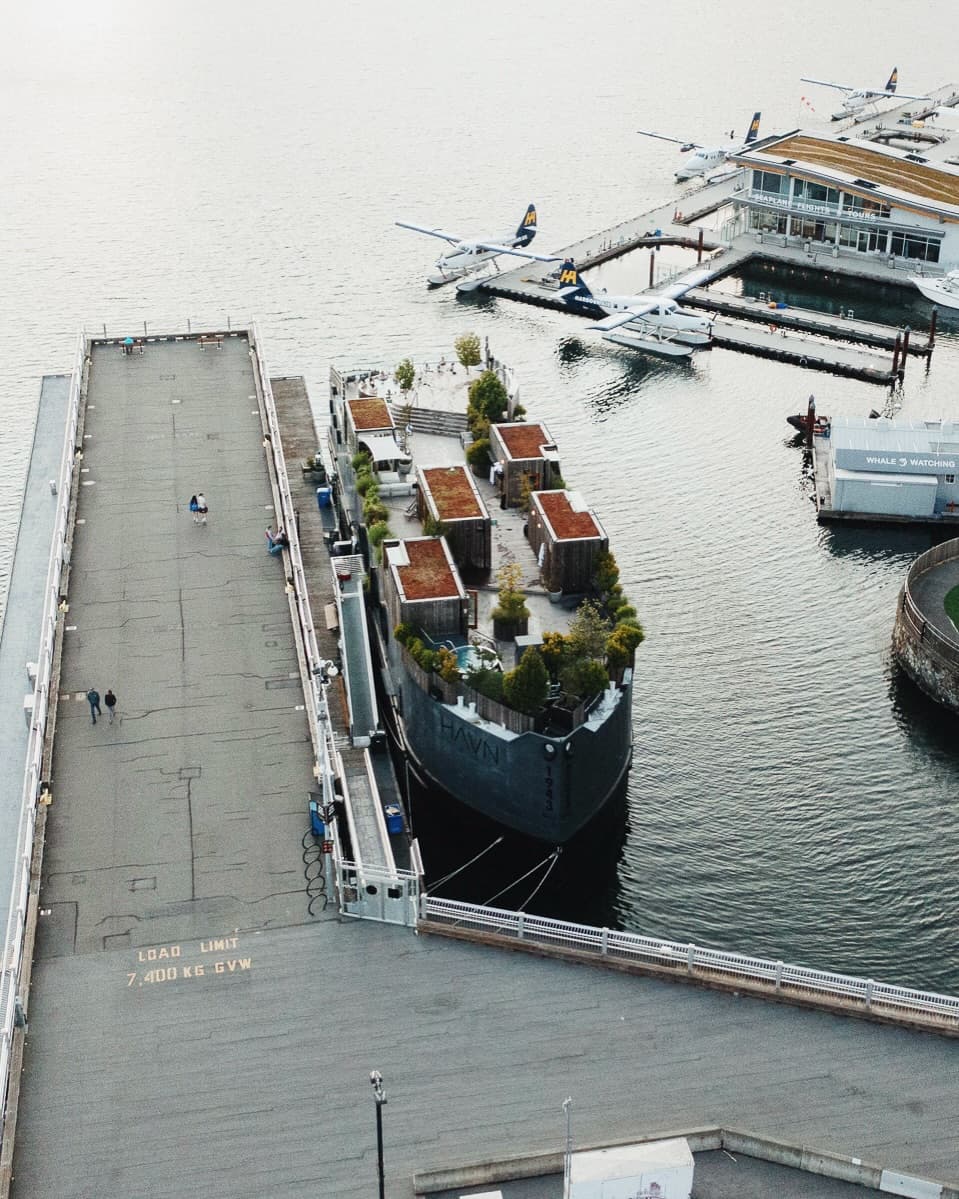 Aerial view of HAVN Harbour Sauna docked in Victoria's Inner Harbour with green roofs, soaking tubs, and seaplanes in the background