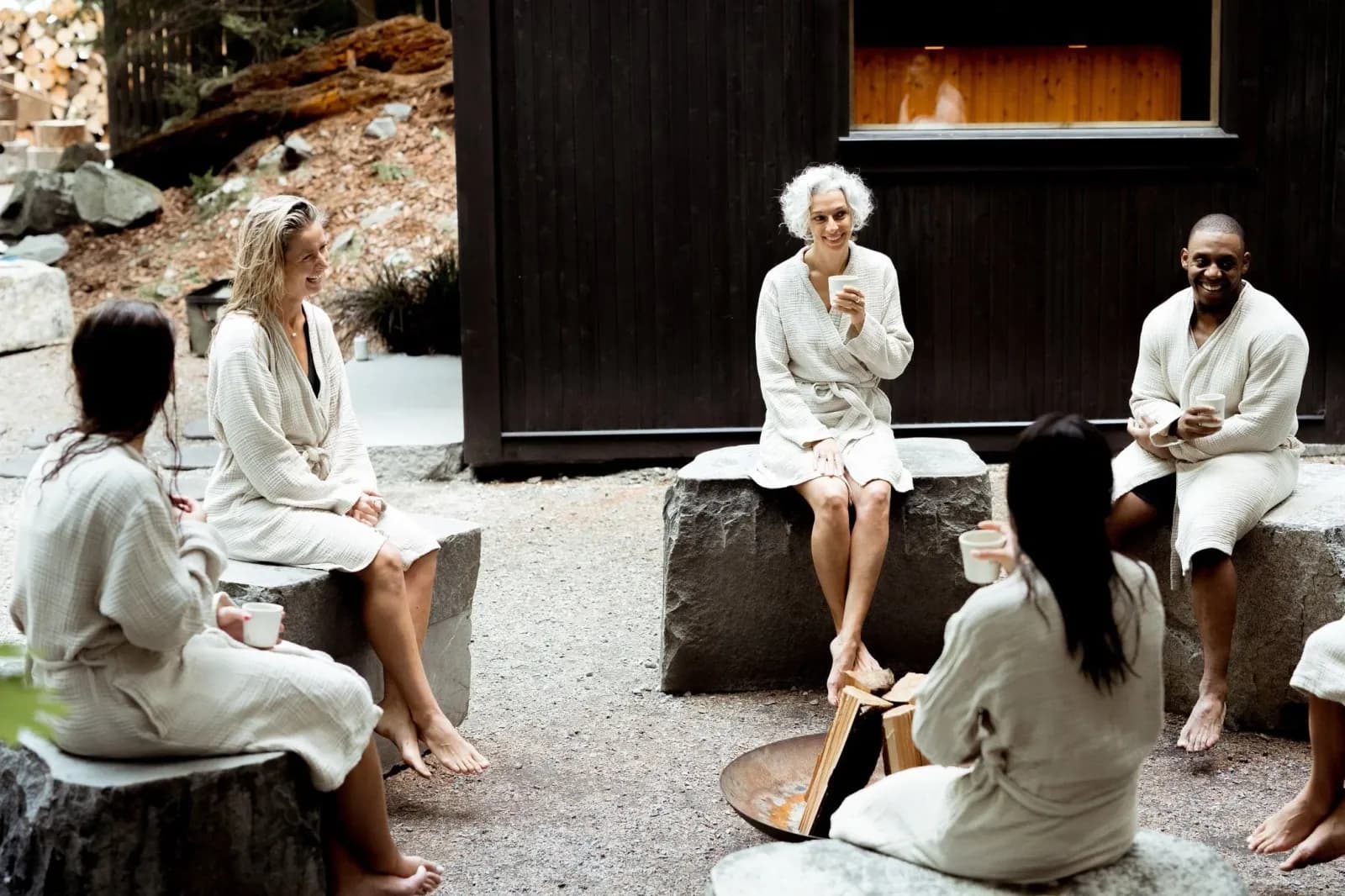 AIKA Spa wood-clad sauna cabin in the Squamish Valley forest with stone seating and guests in robes