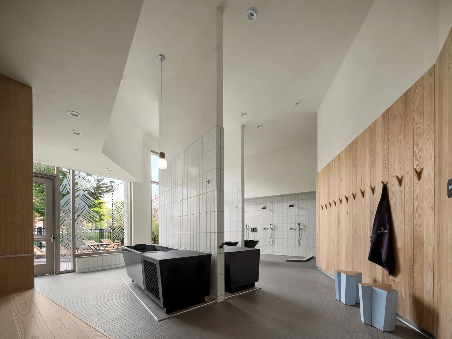 BASK Detroit modern wellness space with cold plunge tubs, showers, and wood accent wall