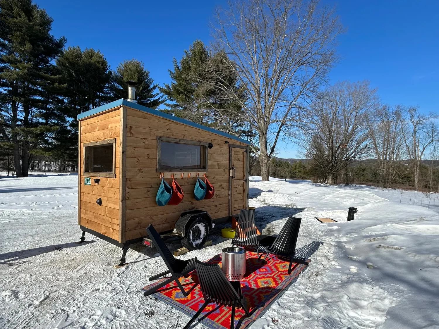 Brattleboro Sauna wood-fired mobile sauna trailer with outdoor chairs and fire pit in a snowy Vermont field