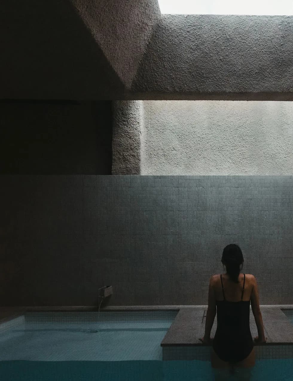 Guest seated at the edge of the mineral bath with natural light streaming through the skylight at Capybara Bathing Singapore