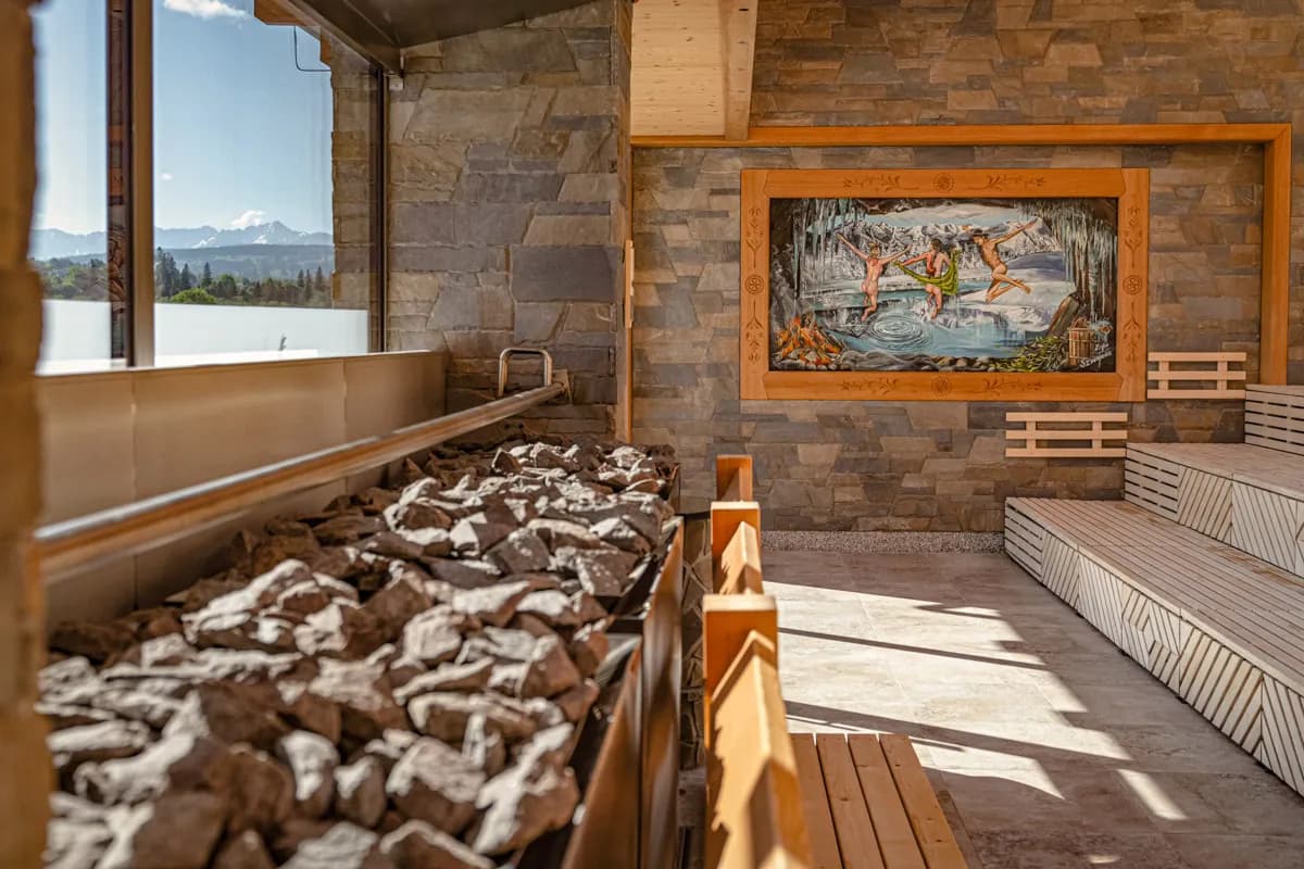 Sauna Pierońska at Chochołowskie Termy with large stone heater, wooden benches, decorative mural, and panoramic window overlooking the Tatra Mountains