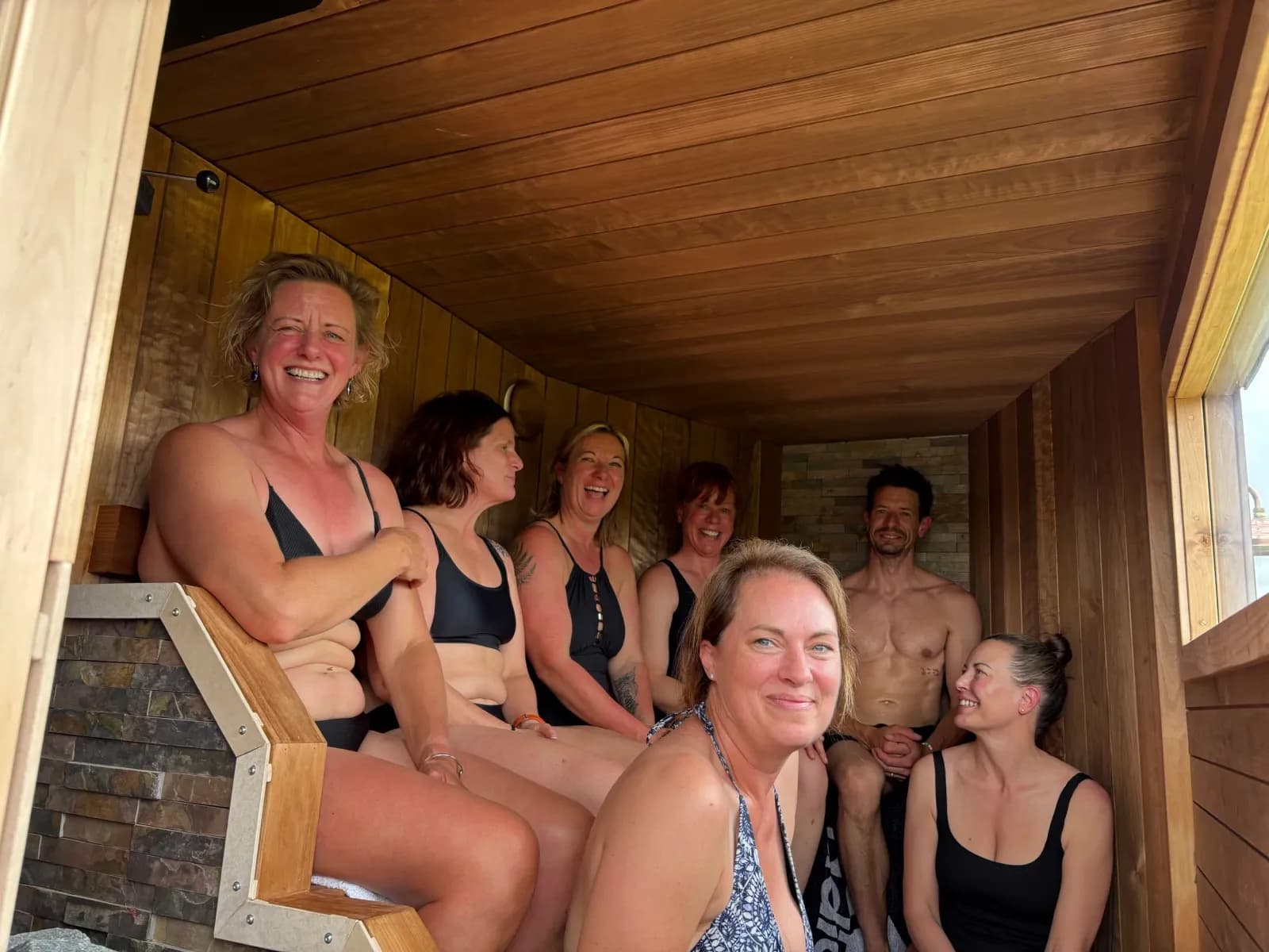 Group of people sitting inside a wooden sauna at Happi Sauna