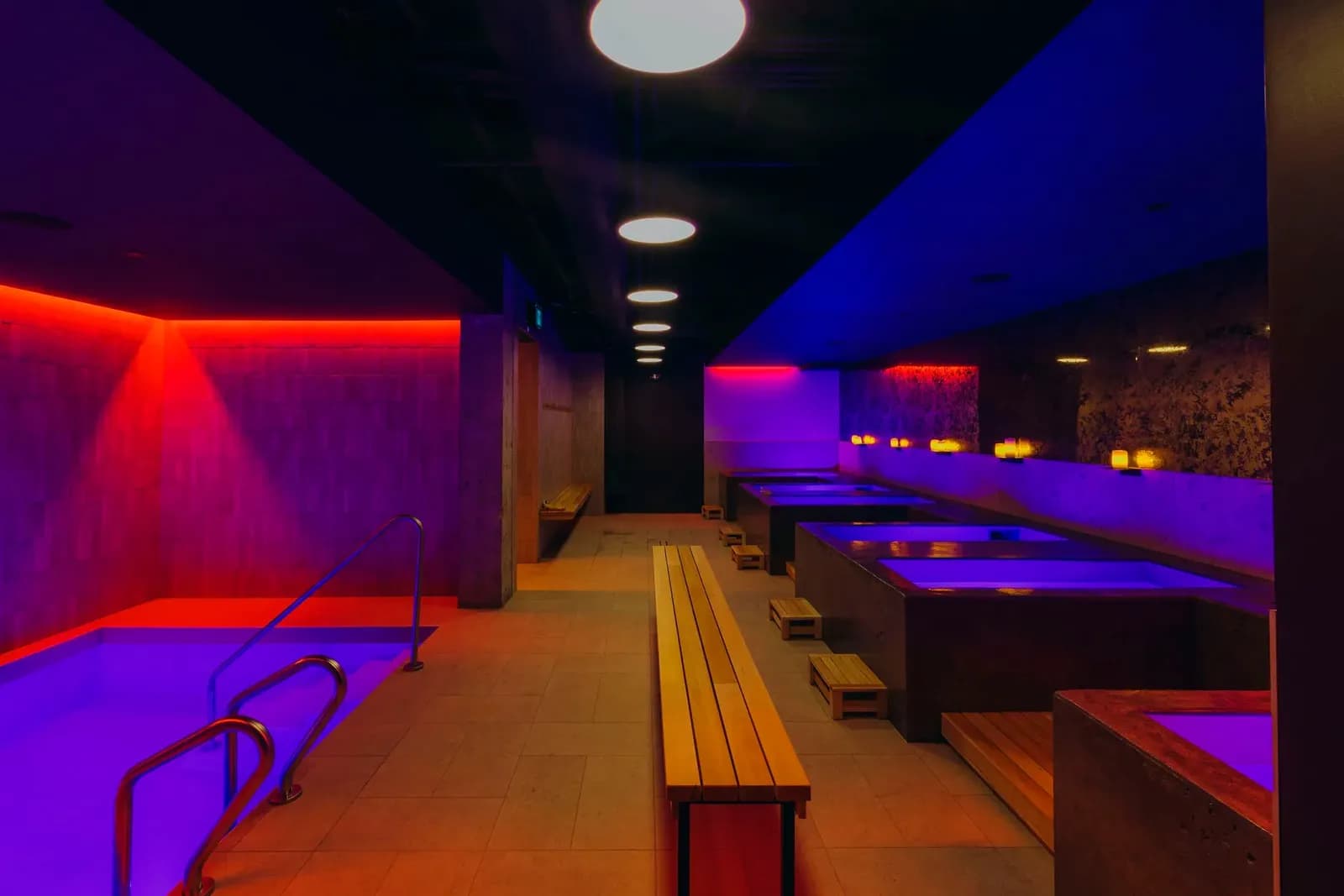 Neon-lit bathhouse with cold plunge pools and wooden benches at JOY Wellness Club, Montréal