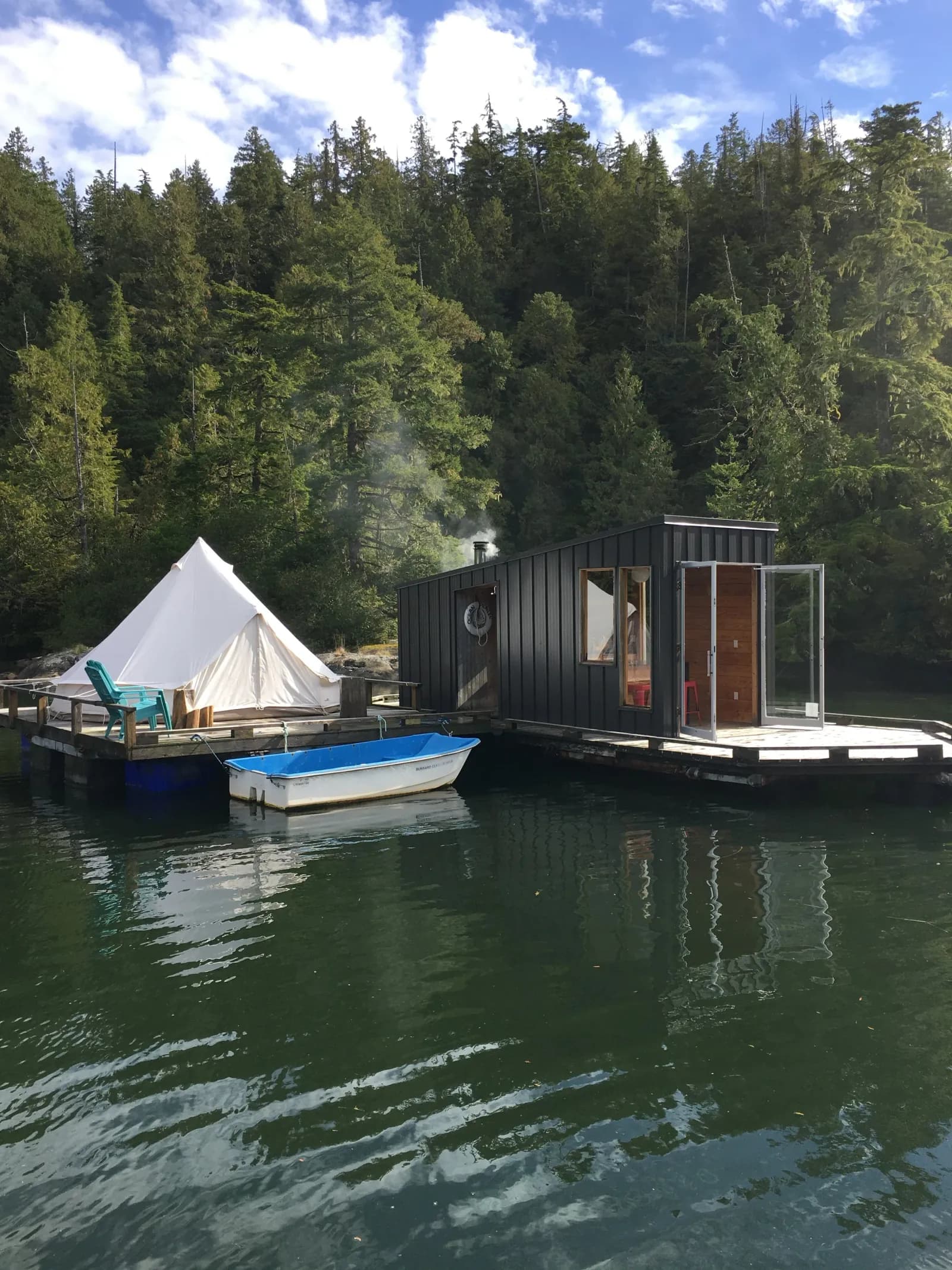 The Lagoon Float Camp floating platform with wood-fired sauna cabin, canvas bell tent, and a small boat on the water