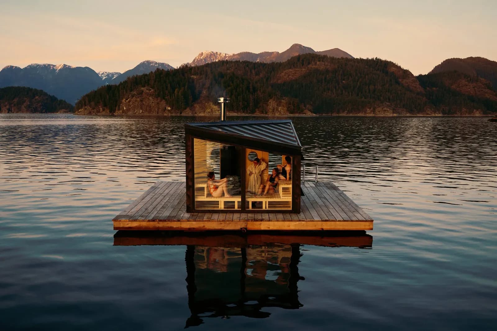 Refuge Sauna's floating wood cabin moored on its private dock at dusk in Desolation Sound with the Coast Mountains behind