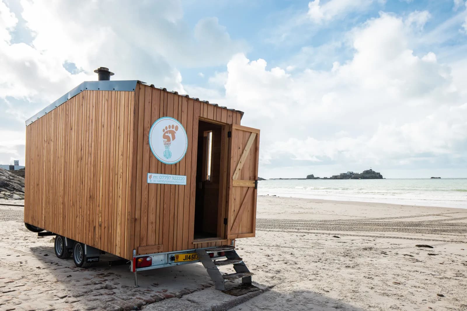 Sandy Toes Sauna mobile wood-fired sauna on St Brelade's Bay beach with Elizabeth Castle visible in the background