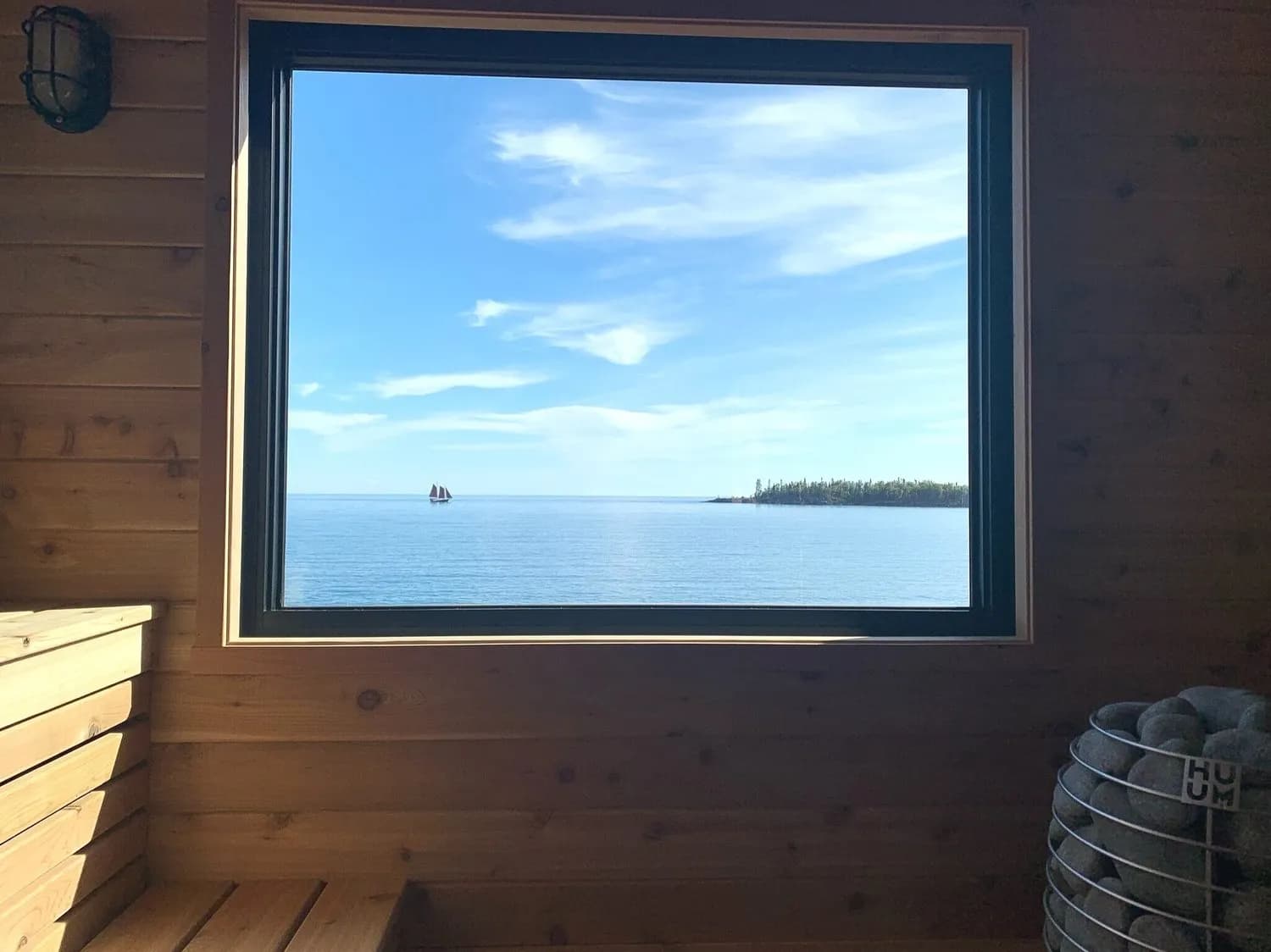 Cedar-lined interior of the Sisu + Löyly sauna with a large picture window overlooking Lake Superior and a stone-filled electric heater