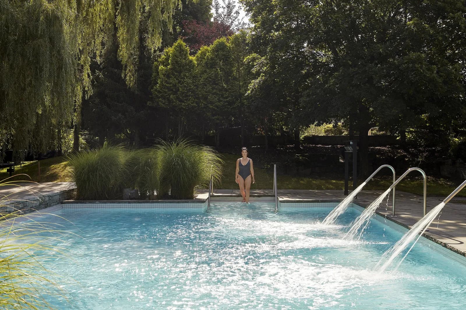 Temperate outdoor pool with thermal waterfalls under weeping willows at Strøm Mont-Saint-Hilaire