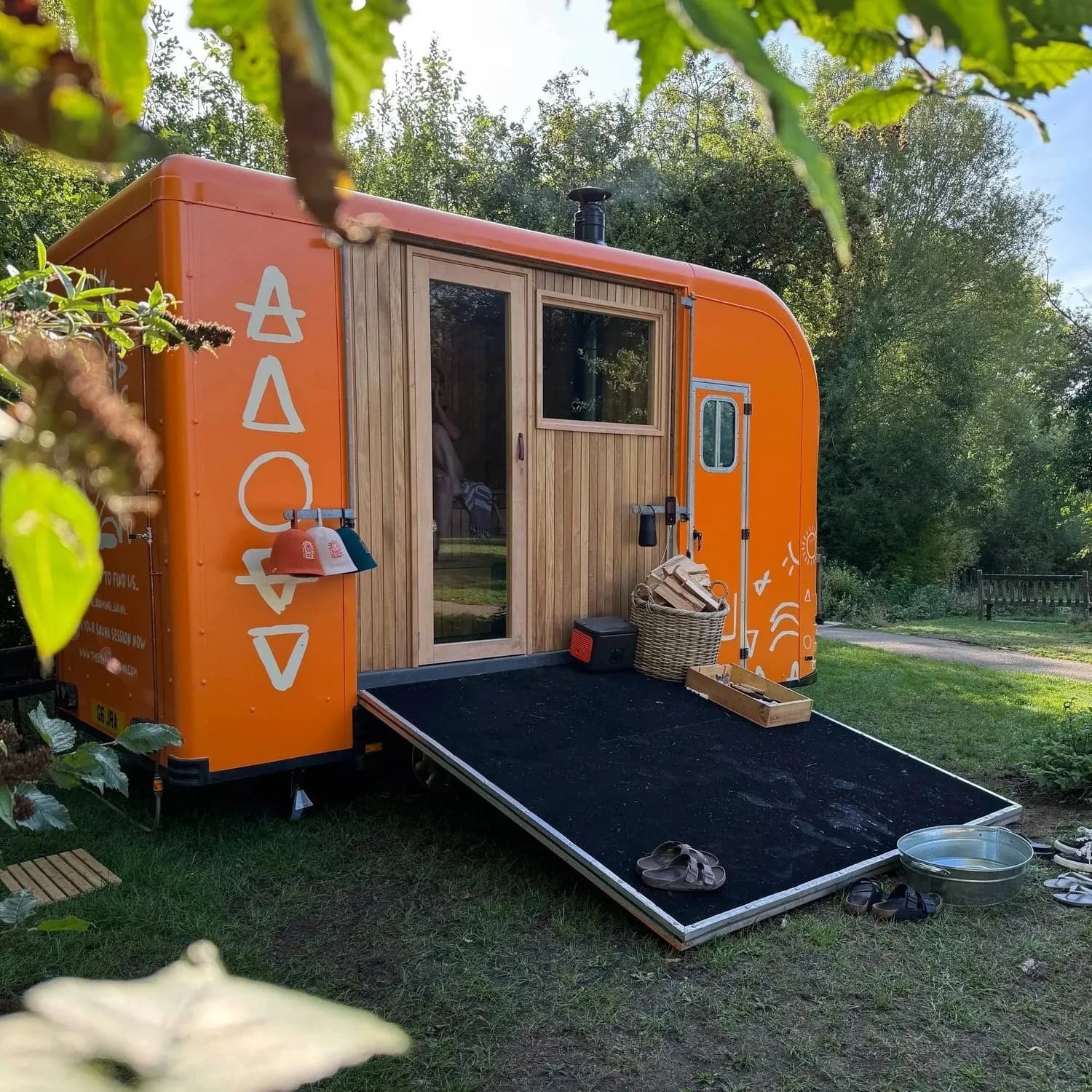 The Roaming Sauna's distinctive orange mobile wood-fired sauna trailer set up in a green Suffolk countryside setting
