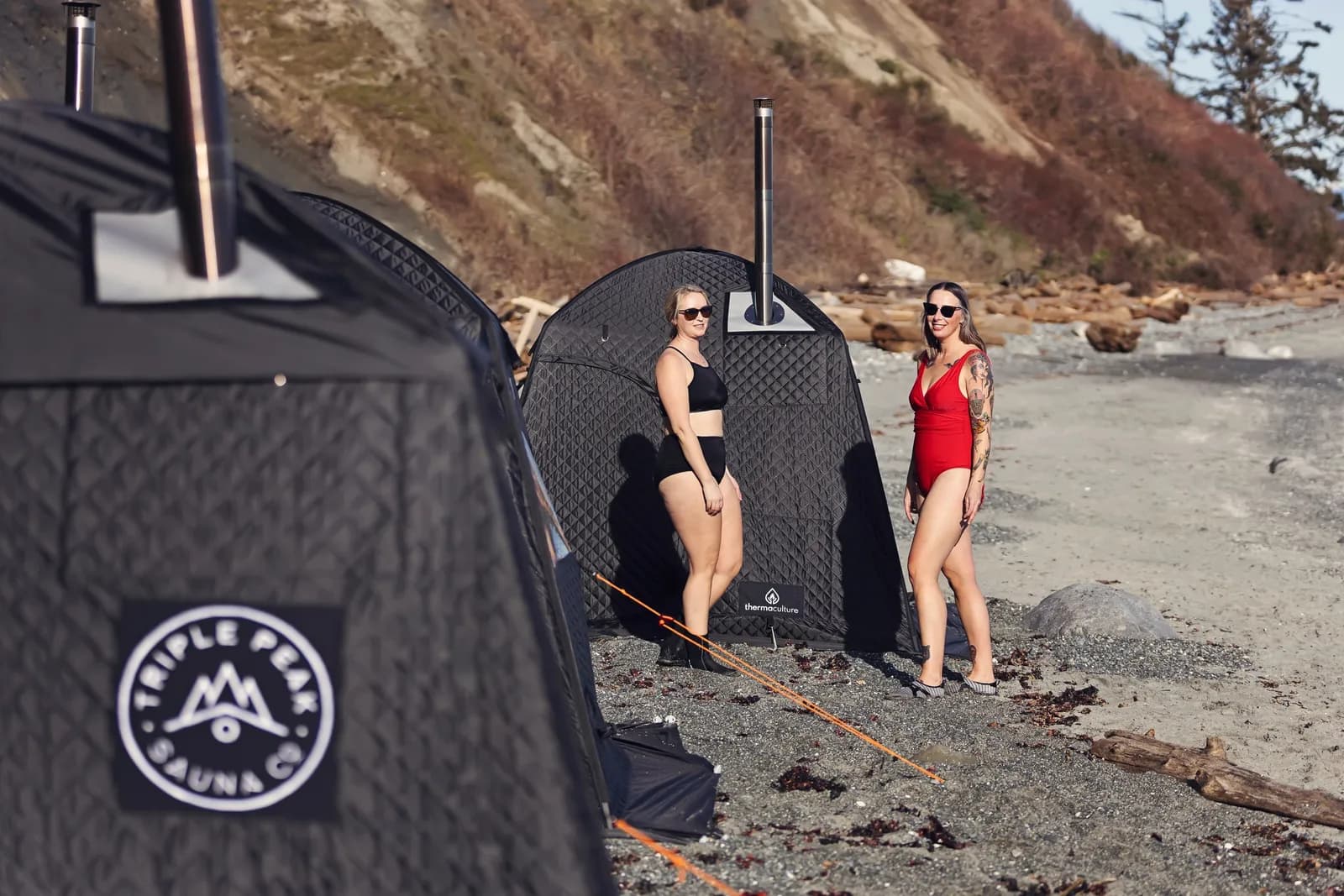 Two Triple Peak Sauna Co. branded tent saunas set up along a Vancouver Island shoreline