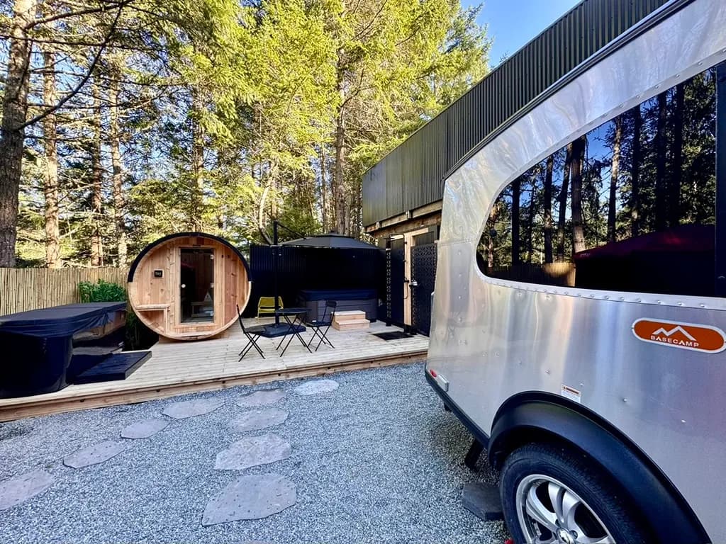WOODS Nordic Spa outdoor area showing cedar barrel sauna, Airstream basecamp, and forest canopy setting on Pender Island