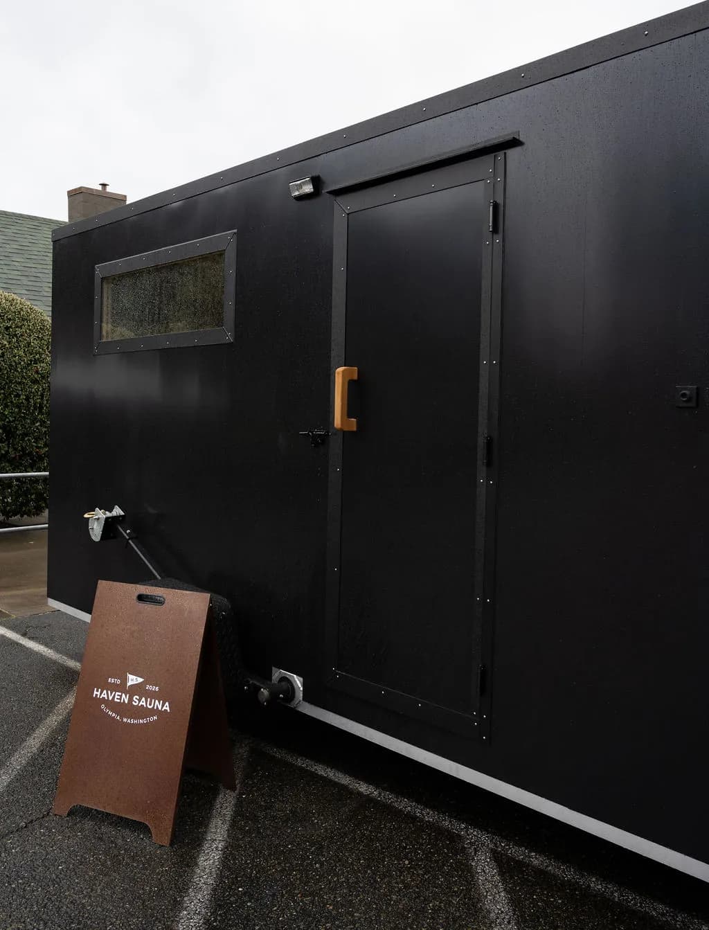 Black Haven Sauna mobile sauna trailer with a Haven Sauna sandwich-board sign in Olympia, Washington