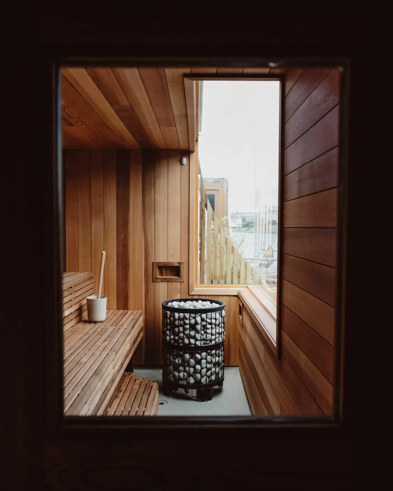 Cedar-lined sauna interior with HUUM stone heater and harbour view through the window