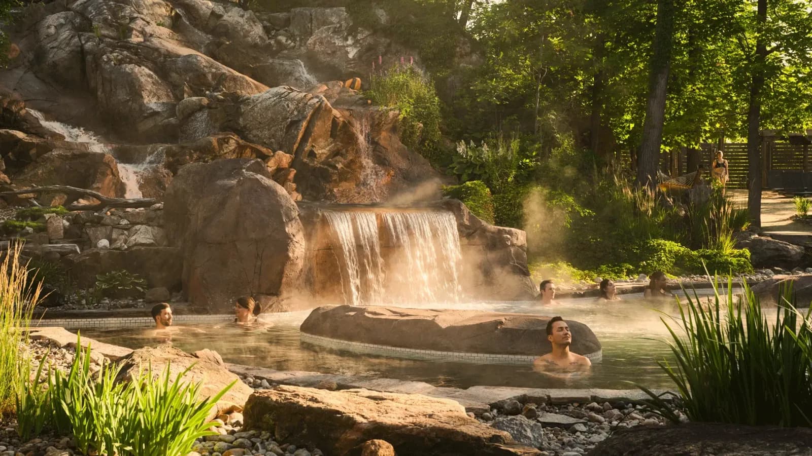 Guests soaking in natural rock pools surrounded by lush greenery and steam at Nordik Spa-Nature Chelsea