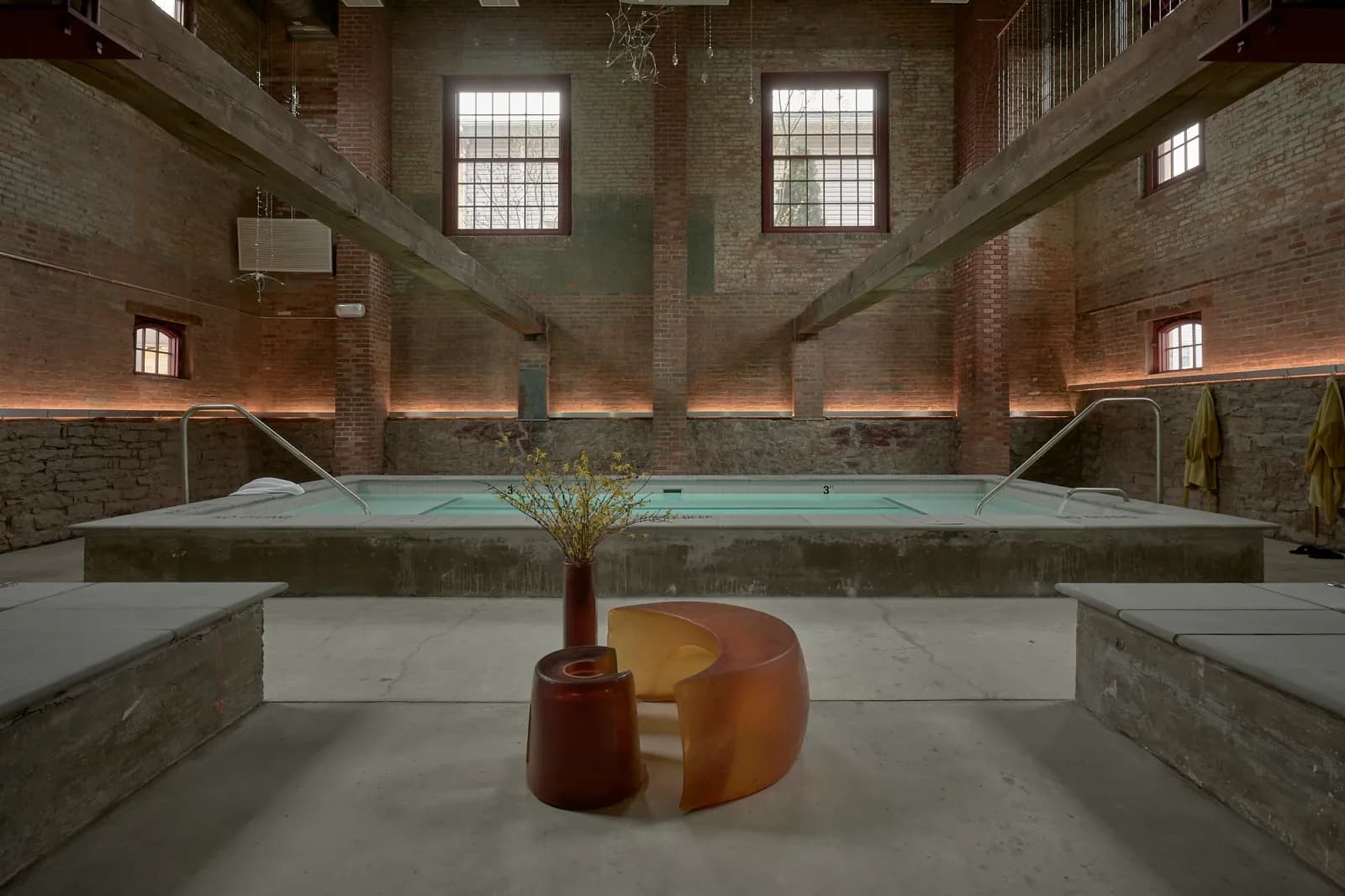 The communal thermal pool at Pocketbook Hudson Baths set in a soaring 1885 brick-and-timber warehouse with arched windows