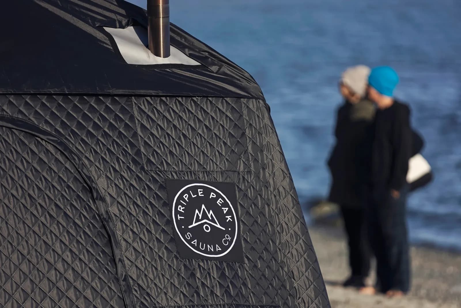 Triple Peak Sauna Co. branded wood-fired pop-up tent sauna on a pebble beach